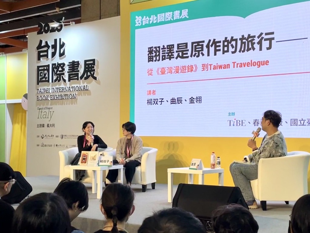 Lin King and Yáng Shuāng-zǐ converse on stage at TiBE, in front of a backdrop that reads in Traditional Chinese: ‘Translation is the original work on a journey: From《臺灣漫遊錄》to Taiwan Travelogue’ (translation mine).